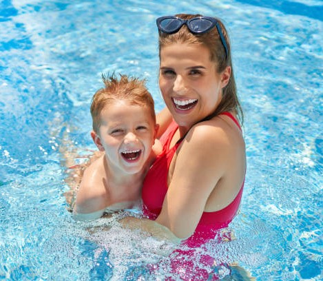 Picture of cute boy with his mother playing in a pool of water during the summer